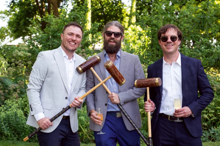Three ben holding croquet clubs and champagne glasses