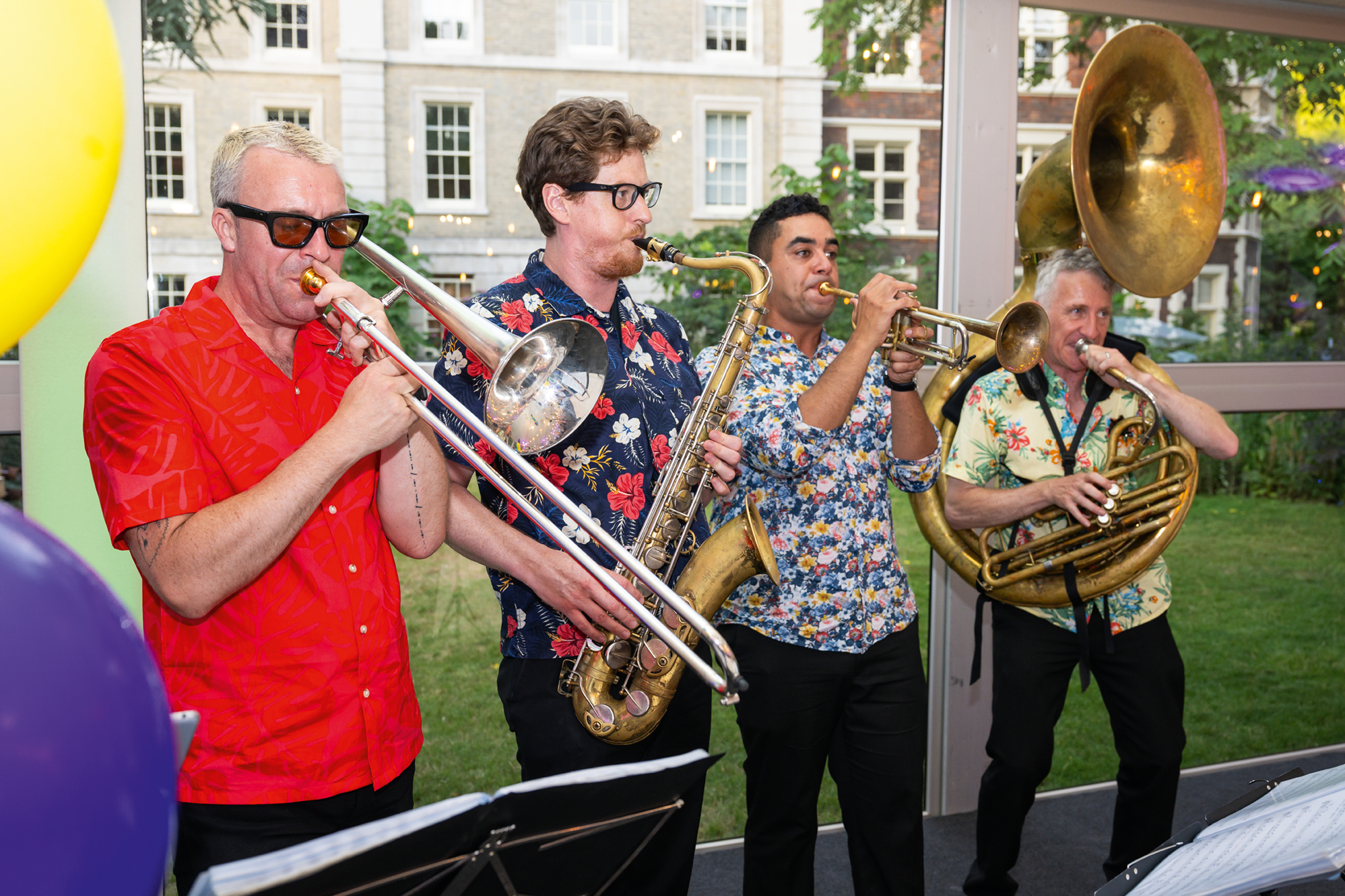 4 men playing brass instruments in colourful shirts